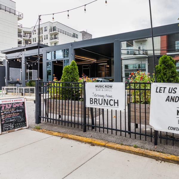Exterior of Music Row Bar & Grill with outdoor patio, string lights, and signs for brunch and private events.