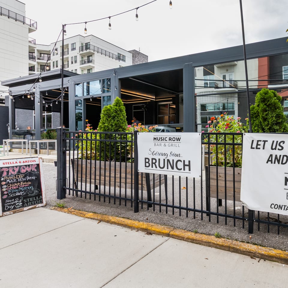 Exterior of Music Row Bar & Grill with outdoor patio, string lights, and signs for brunch and private events.
