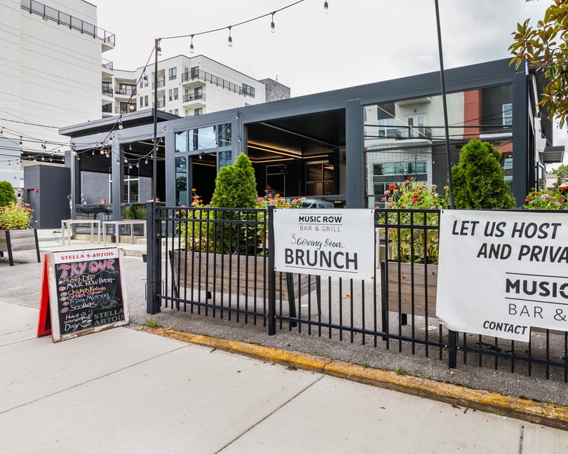 Exterior of Music Row Bar & Grill with outdoor patio, string lights, and signs for brunch and private events.