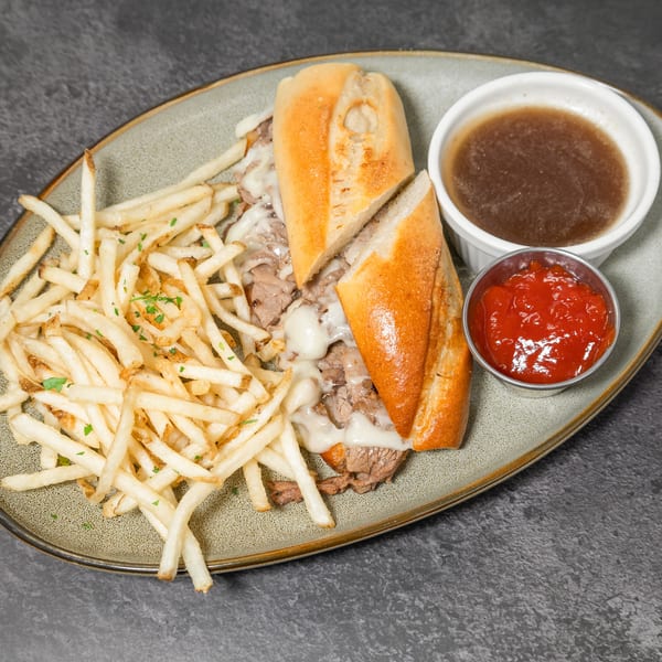 Philly cheesesteak sandwich with fries, au jus, and ketchup on a speckled plate.