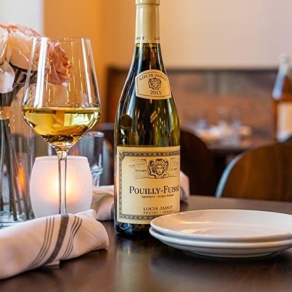 A bottle of Pouilly-Fuissé wine, a glass of white wine, and a floral centerpiece on a restaurant table.