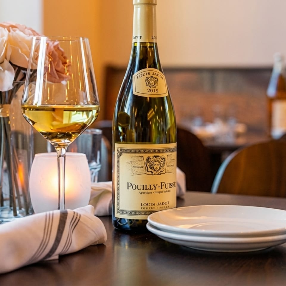 A bottle of Pouilly-Fuissé wine, a glass of white wine, and a floral centerpiece on a restaurant table.