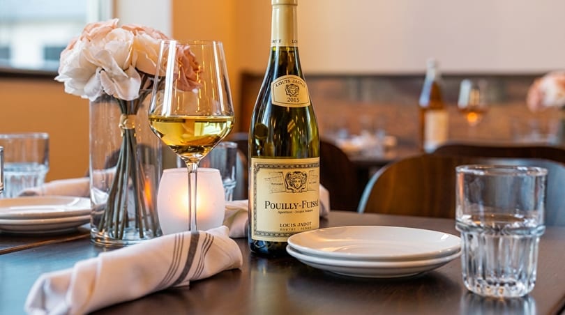 A bottle of Pouilly-Fuissé wine, a glass of white wine, and a floral centerpiece on a restaurant table.