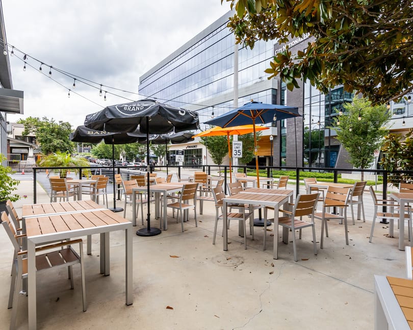 Outdoor restaurant patio with tables, chairs, and umbrellas, against an urban building backdrop.