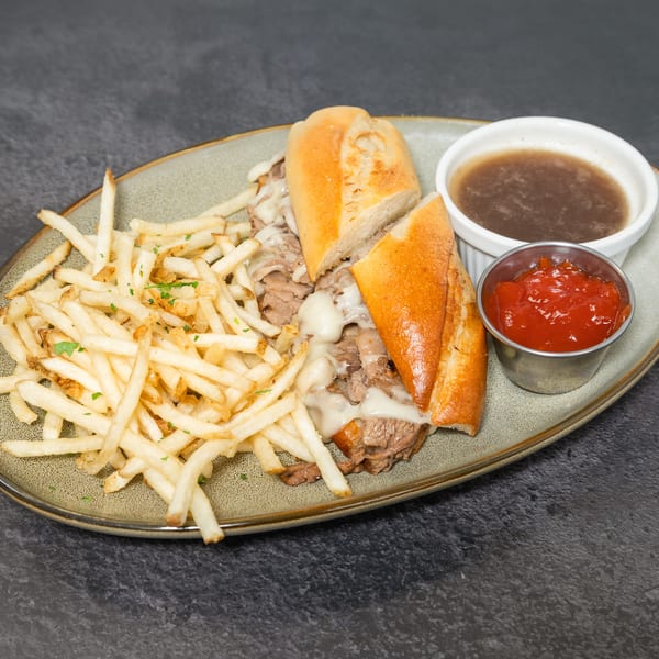 Cheesy French dip sandwich with golden fries, au jus, and ketchup on a grey plate.