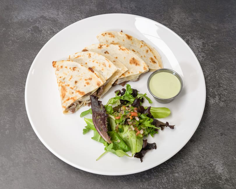 Four quesadilla slices with melted cheese and meat, served with a side salad and green dipping sauce.