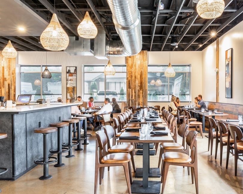 Modern restaurant interior with a bar, dining tables, and patrons enjoying meals.
