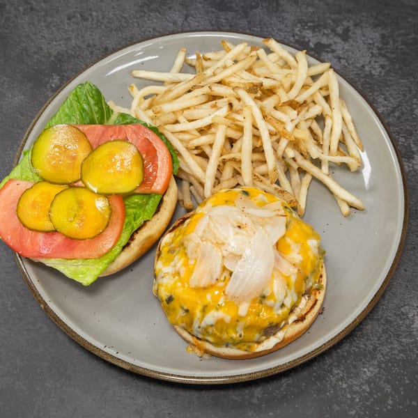 Open-faced cheeseburger with grilled onions, lettuce, tomato, pickles, and a side of crispy french fries.